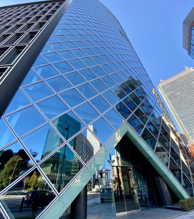 Dramatic upward view of a modern glass skyscraper reflecting a vibrant cityscape.