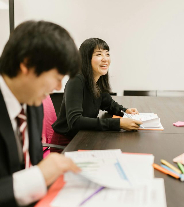 A businesswoman smiling during a meeting alongside colleagues in an office setting.